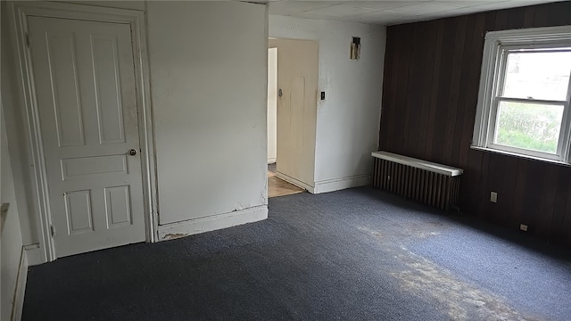 unfurnished room with radiator, wood walls, and carpet flooring