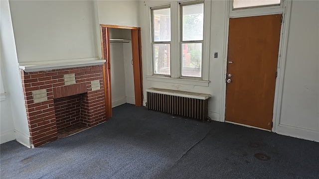 unfurnished living room featuring a fireplace, dark carpet, and radiator heating unit