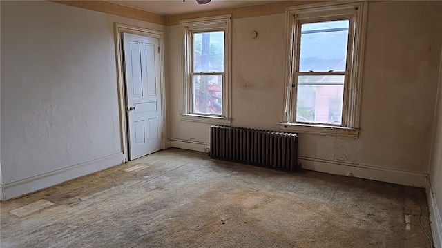 spare room with radiator heating unit, ceiling fan, and light carpet