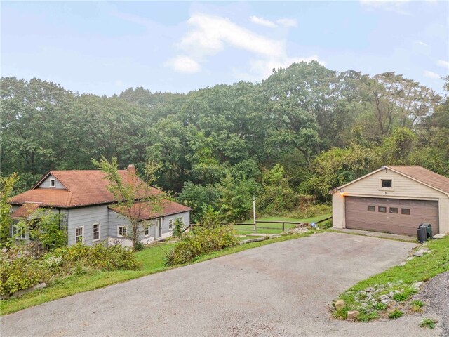 exterior space featuring an outbuilding, a detached garage, a wooded view, and a chimney