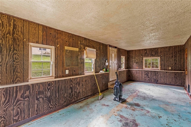 unfurnished room with a textured ceiling, wooden walls, and a wealth of natural light