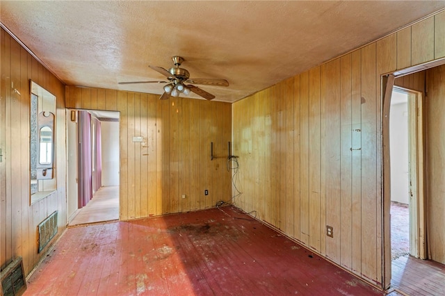 spare room featuring a textured ceiling, light hardwood / wood-style floors, wood walls, and ceiling fan