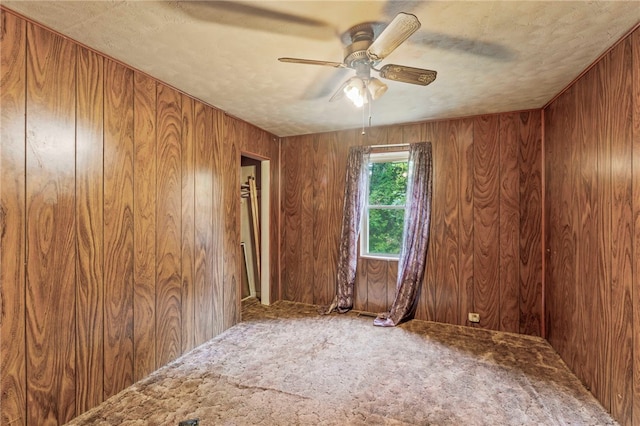 carpeted empty room with a textured ceiling, wood walls, and ceiling fan