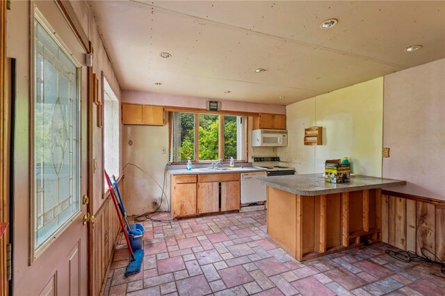 kitchen with a sink, white appliances, a peninsula, brown cabinetry, and brick floor