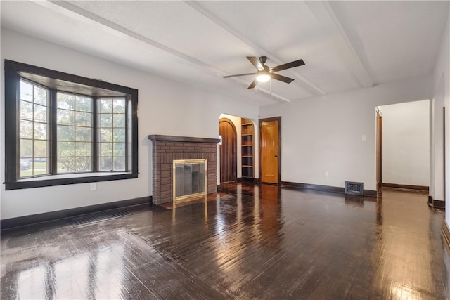 unfurnished living room featuring dark hardwood / wood-style floors, beamed ceiling, a fireplace, and ceiling fan