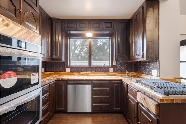 kitchen featuring dark wood-type flooring, backsplash, stainless steel appliances, and dark brown cabinetry