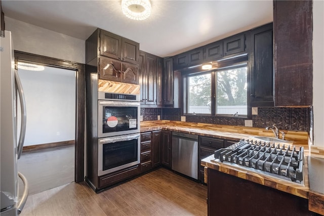 kitchen featuring appliances with stainless steel finishes, wood-type flooring, backsplash, dark brown cabinets, and wooden counters