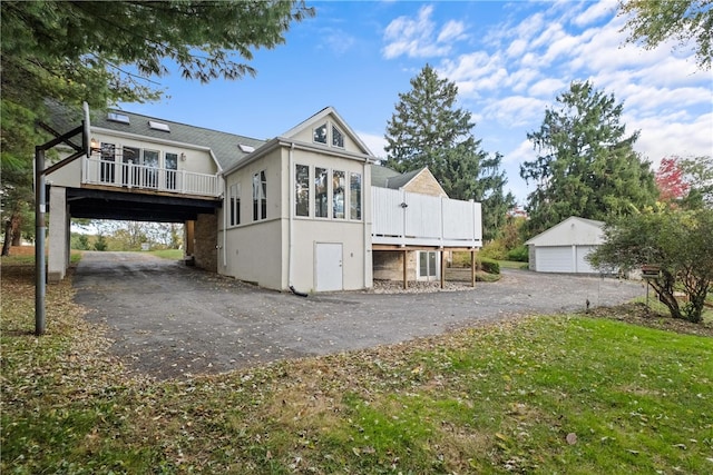 back of house featuring a wooden deck, an outbuilding, a garage, and a lawn