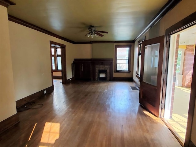 unfurnished living room with a brick fireplace, ceiling fan, dark wood-type flooring, and crown molding