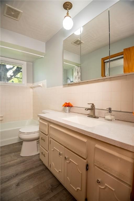 full bathroom featuring tile walls, hardwood / wood-style flooring, tasteful backsplash, vanity, and toilet