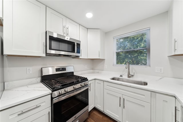 kitchen with light stone counters, white cabinets, sink, dark wood-type flooring, and stainless steel appliances