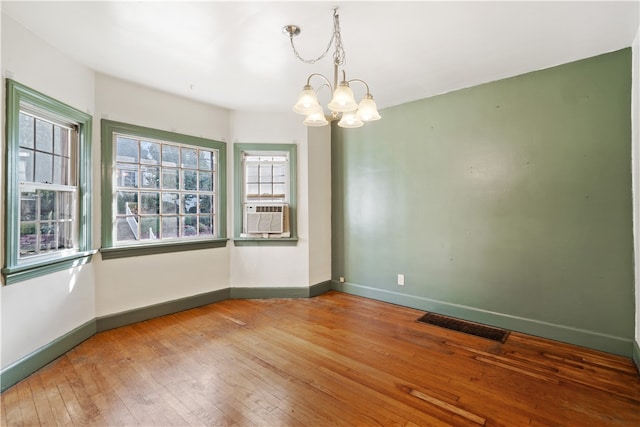 unfurnished room featuring wood-type flooring, an inviting chandelier, and cooling unit