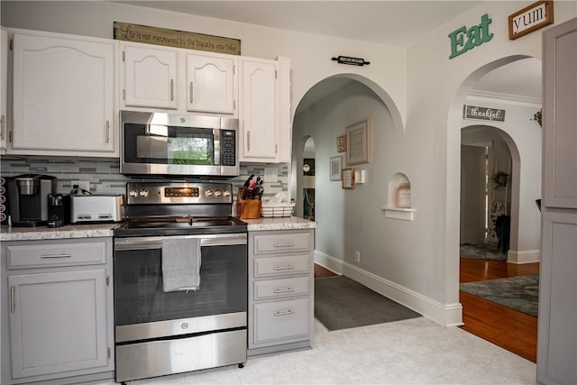 kitchen with appliances with stainless steel finishes, light hardwood / wood-style floors, white cabinets, backsplash, and ornamental molding