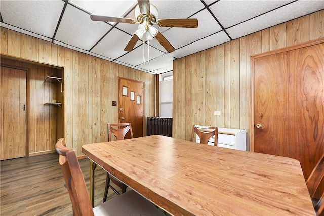 dining room featuring a paneled ceiling, wood walls, dark hardwood / wood-style floors, and ceiling fan