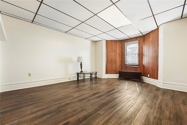 unfurnished living room with radiator, wood walls, dark hardwood / wood-style floors, and a paneled ceiling