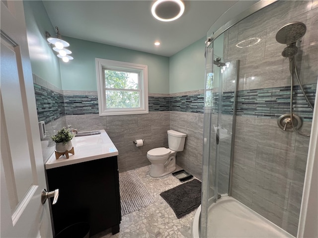 bathroom with a shower with door, vanity, toilet, and tile walls