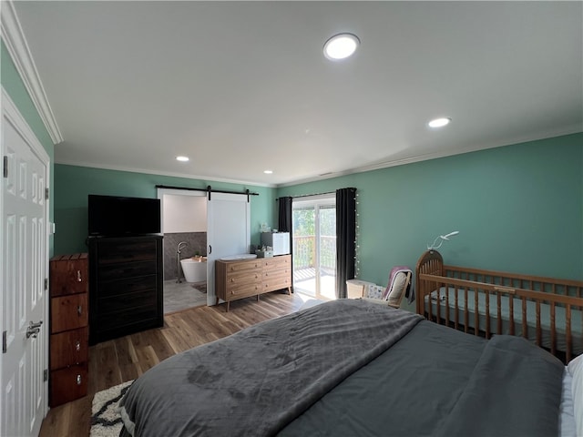 bedroom featuring a barn door, hardwood / wood-style flooring, access to exterior, ornamental molding, and ensuite bath