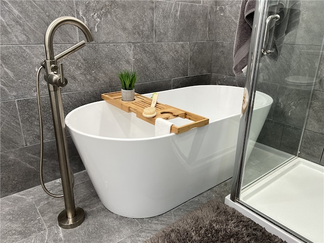 bathroom featuring shower with separate bathtub and tile walls