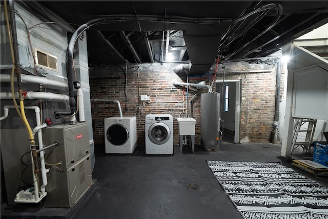 basement with heating unit, sink, separate washer and dryer, water heater, and brick wall