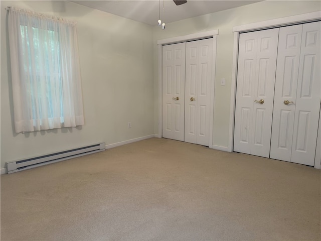 unfurnished bedroom with light carpet, a baseboard heating unit, and multiple closets