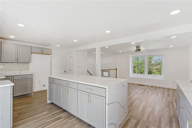 kitchen with gray cabinetry, backsplash, a center island, and light hardwood / wood-style flooring