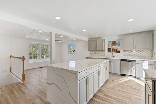 kitchen with light stone countertops, light hardwood / wood-style floors, a center island, and stainless steel dishwasher