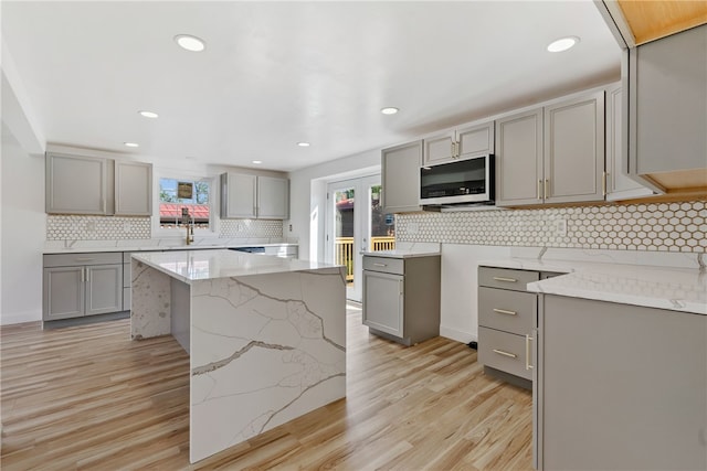 kitchen with light stone counters, gray cabinets, light hardwood / wood-style floors, and tasteful backsplash