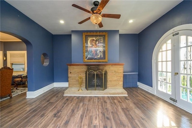 unfurnished living room featuring a wealth of natural light, dark hardwood / wood-style floors, french doors, and a stone fireplace