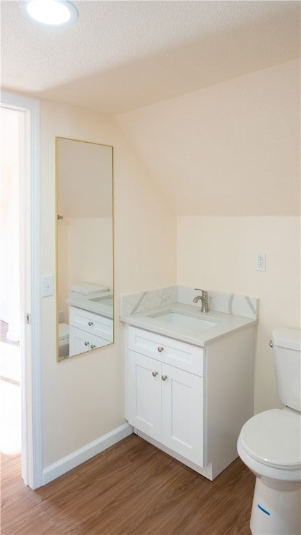 bathroom with wood-type flooring, a textured ceiling, vaulted ceiling, vanity, and toilet