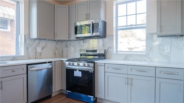 kitchen featuring gray cabinets, stainless steel appliances, backsplash, and dark wood-type flooring