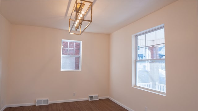 spare room featuring a notable chandelier, a healthy amount of sunlight, and dark hardwood / wood-style flooring