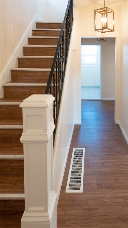 stairway featuring wood-type flooring and an inviting chandelier