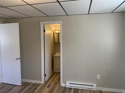 unfurnished bedroom with ensuite bathroom, wood-type flooring, and baseboard heating