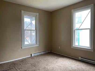 carpeted spare room with a baseboard heating unit