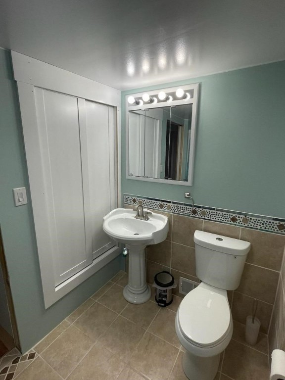 bathroom featuring tile patterned floors, toilet, and tile walls