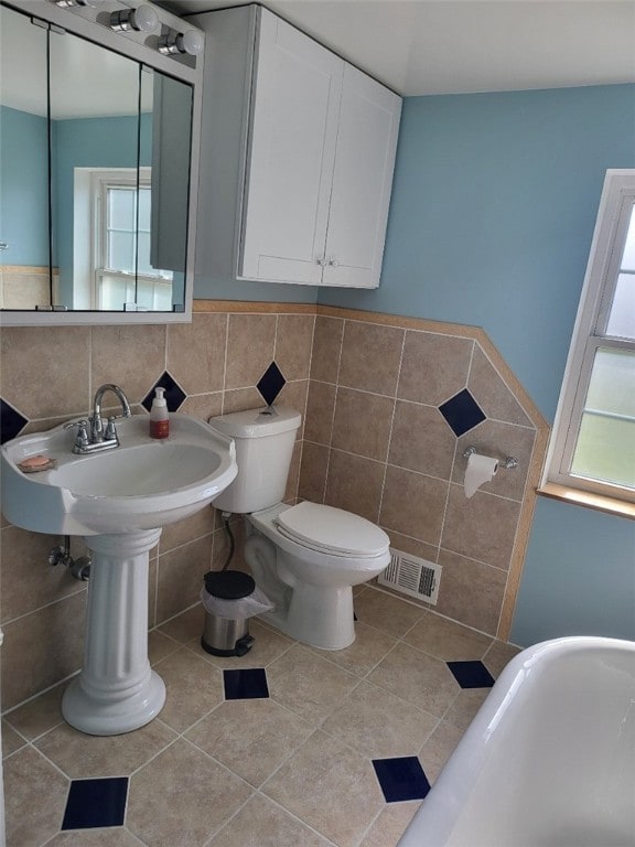 bathroom featuring tile patterned floors, a bath, tile walls, and toilet