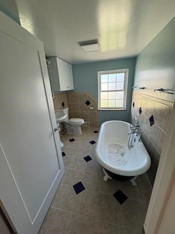 bathroom with sink, tile patterned flooring, toilet, a bathtub, and tile walls