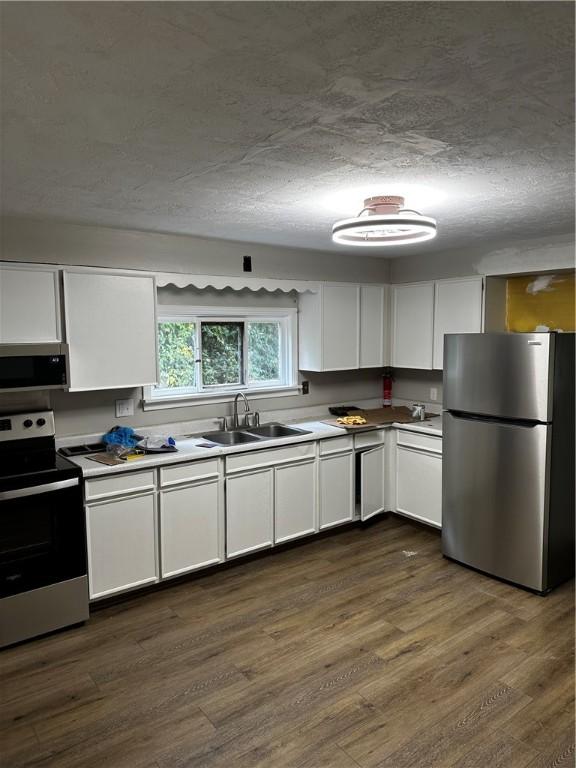 kitchen with white cabinetry, sink, stainless steel appliances, dark hardwood / wood-style floors, and a textured ceiling