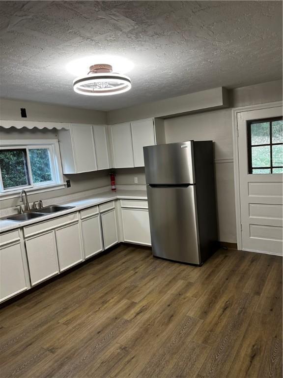 kitchen with stainless steel fridge, a textured ceiling, dark wood-type flooring, sink, and white cabinets