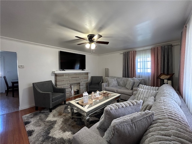 living room with crown molding, a stone fireplace, dark hardwood / wood-style flooring, and ceiling fan