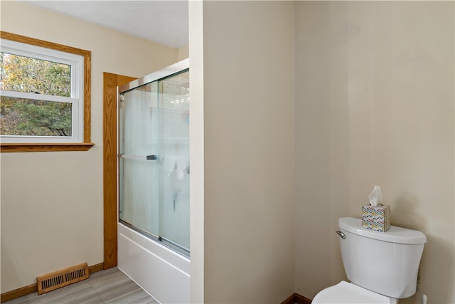 bathroom with hardwood / wood-style floors, shower / bath combination with glass door, and toilet