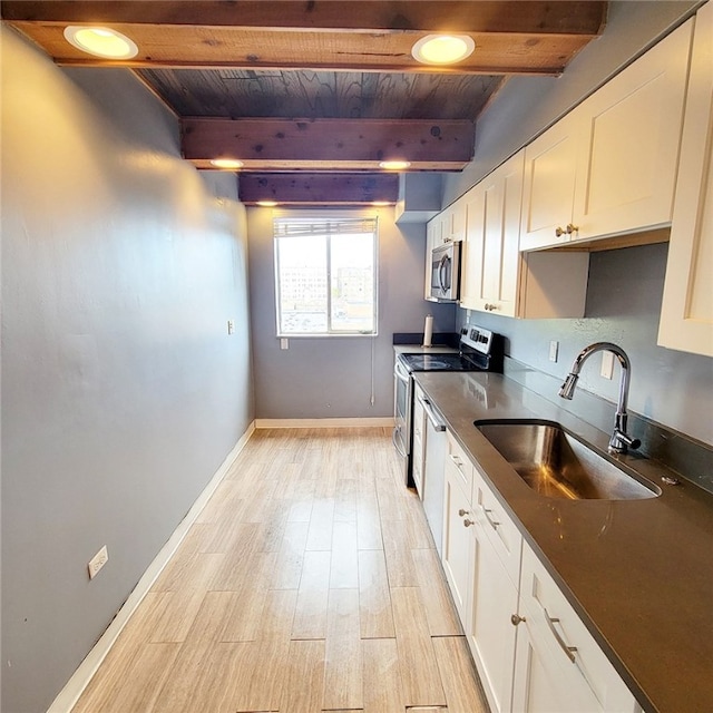 kitchen featuring beamed ceiling, appliances with stainless steel finishes, white cabinetry, and sink