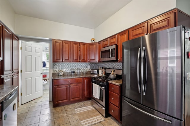 kitchen with stainless steel appliances, backsplash, light tile patterned floors, and dark stone counters