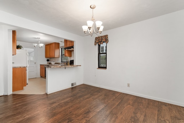 kitchen with dark hardwood / wood-style flooring, kitchen peninsula, a breakfast bar area, white fridge, and an inviting chandelier