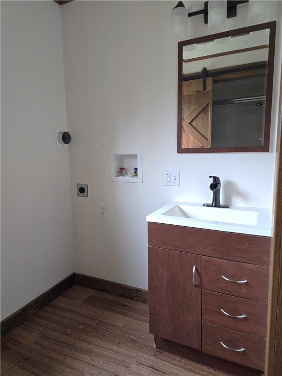 washroom featuring sink, hookup for an electric dryer, hookup for a washing machine, a barn door, and dark hardwood / wood-style flooring