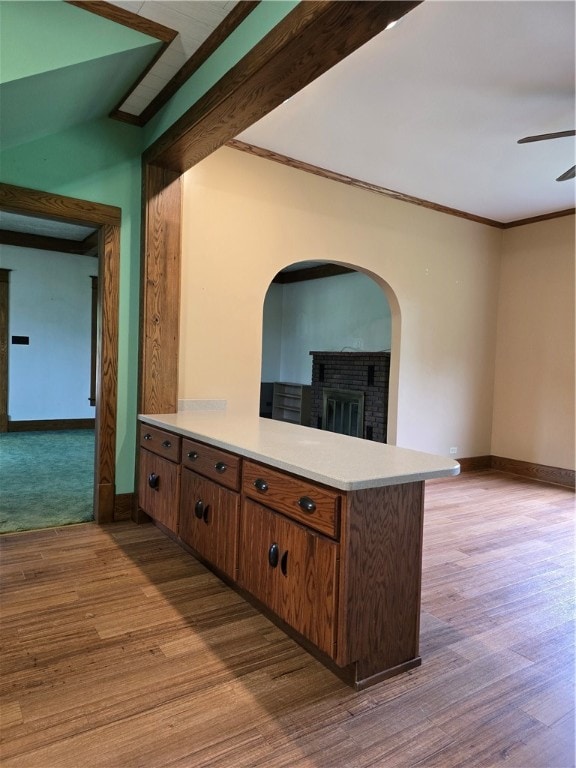 kitchen with light wood-type flooring, kitchen peninsula, a fireplace, and crown molding