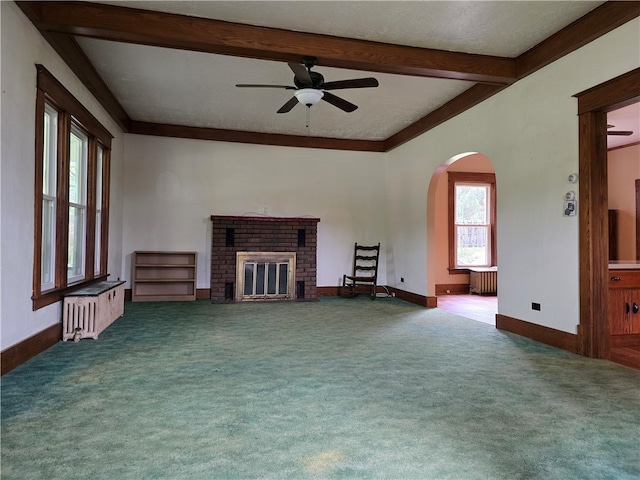 unfurnished living room with radiator heating unit, a brick fireplace, dark colored carpet, and beamed ceiling