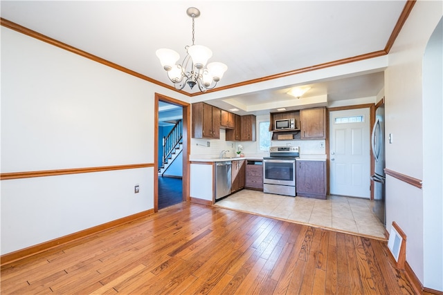 kitchen with hanging light fixtures, an inviting chandelier, crown molding, light hardwood / wood-style floors, and appliances with stainless steel finishes