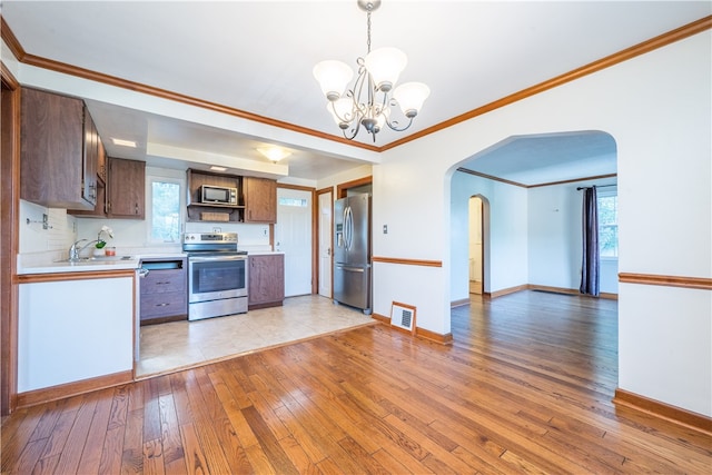 kitchen with appliances with stainless steel finishes, light wood-type flooring, crown molding, pendant lighting, and a chandelier