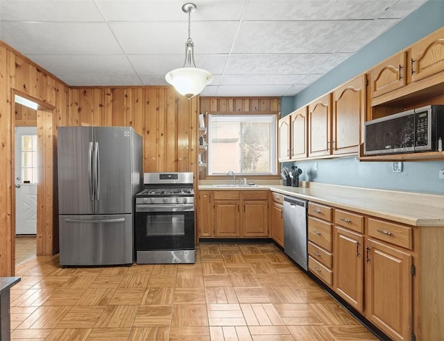 kitchen with pendant lighting, appliances with stainless steel finishes, wood walls, and light parquet flooring